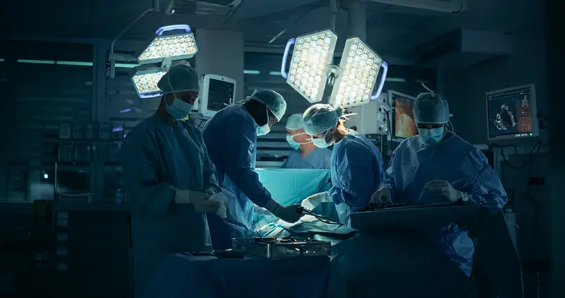 Dressed in Full Protective Gear, Diverse Surgeons and Nurses Coordinate as a Team Around the Operating Table, Saving Life of a Patient with Their Combined Skills and Medical Training