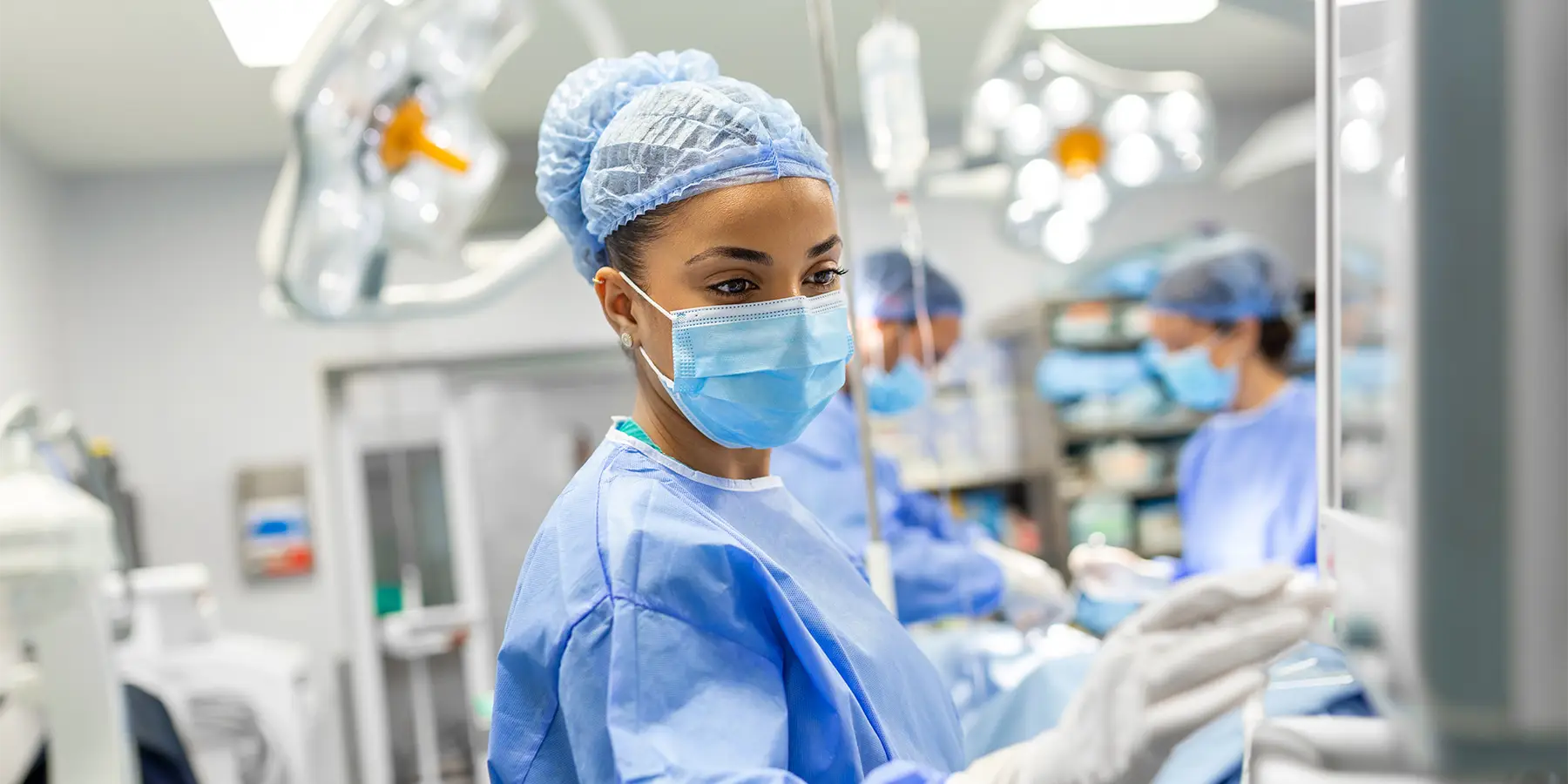 young female doctor in scrubs and a protective face mask preparing an anesthesia machine